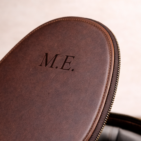 Brown leather case with 'M.E.' monogram on a wooden surface