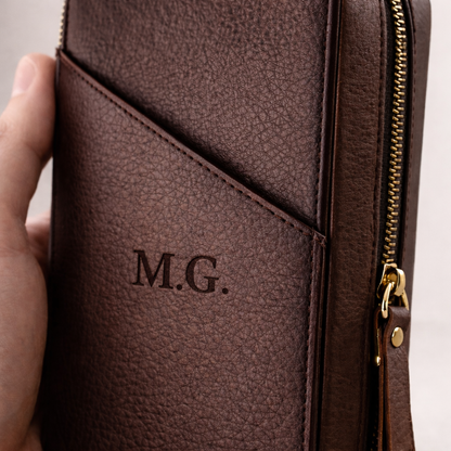 Brown leather wallet with gold zipper held by a hand, featuring initials 'M.G.'