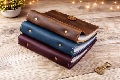 Three leather-bound books stacked on a wooden surface with decorative lights in the background.