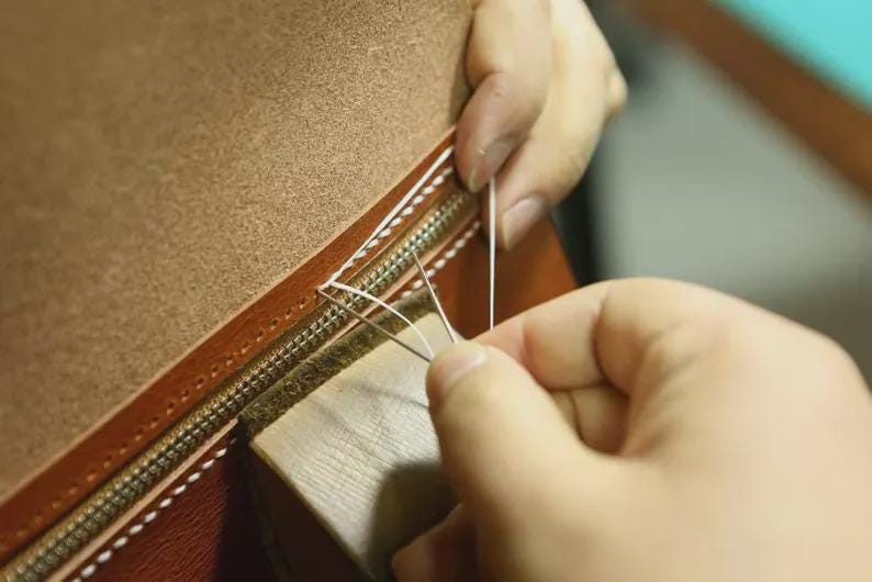 Person sewing a leather-bound book with a needle. leather gifts