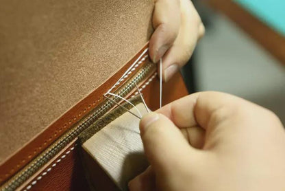 Person sewing a leather-bound book with a needle. leather gifts