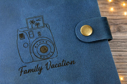 Blue photo album with embroidered camera design and 'Family Vacation' text on a wooden surface. Personalized leather gift. personalized photo album.